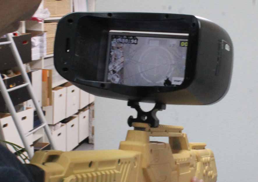 A smartphone is attached to the gun-shaped device’s sights area and used to aim.
